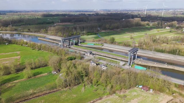 straight canal lock through green farmland tall steel lift gates glass control bridges wooded foreground distant wind turbines spread out town hazy horizon drone view spread-out 