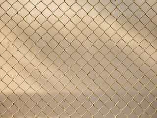 Golden brown chain link fence mesh pattern creating geometric diamond grid texture with soft bokeh...