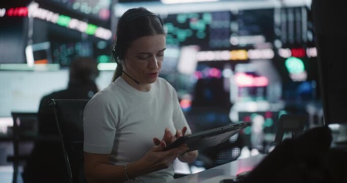 Female Trader Works in Modern Stock Exchange. Woman Interacts With Digital Tablet While Monitoring Complex Market Data Across Large Screens. Concept of Financial Analytics, Professional Multitasking.