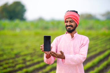 Fototapeta premium Young indian farmer showing smartphone screen at agriculture field