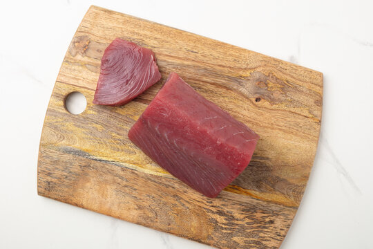 Raw red tuna loin on a wooden cutting board on white 