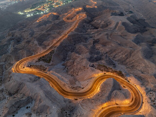 Naklejka premium An aerial view of a winding road through a desert landscape at dusk with city lights in the distance