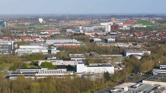 zwijnaarde science park flat roofed research buildings solar arrays serrated skylights dense red suburbs highways rail lines industrial halls wind turbines fade into belgium 