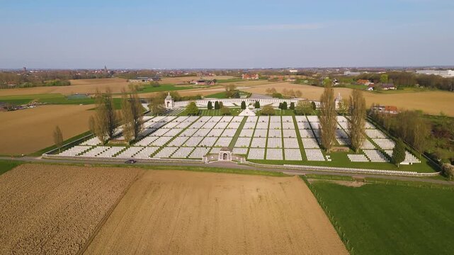 tyne cot cemetery zonnebeke displays thousands uniform white commonwealth headstones precise rows across manicured lawns curved memorial wall tall trees enclose site amid flat wwi 
