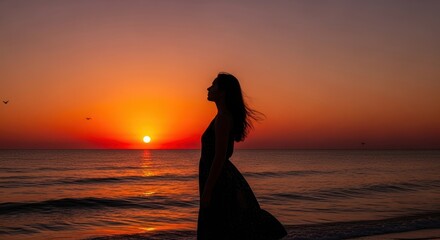 Fototapeta premium Silhouette of a woman enjoying the sunset on the beach.