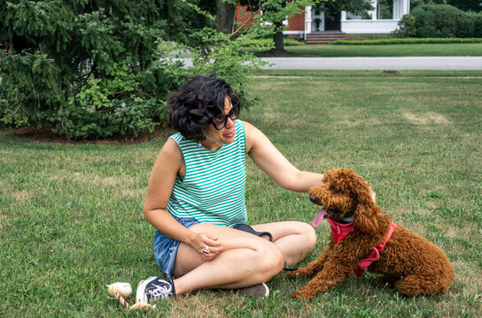 Curly haired woman bonding with her brown poodle dogon green grass in a park
