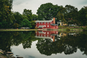 Obraz premium Red barn surrounded by trees reflecting on a calm lake in autumn countryside