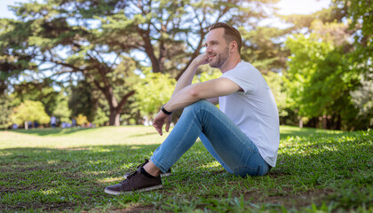 Obraz premium Man relaxing on green grass in a sunny park, enjoying nature with a thoughtful gaze.