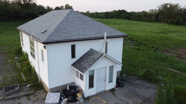 Small abandoned white church house with a Cristian cross in Cambridge, Ontario, Canada. Shot by a drone during late afternoon sunset.
