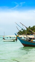 Obraz premium Boats bob gently on crystalline turquoise waters. Sunlight illuminates a sandy beach and lush, green foliage under a clear, blue sky