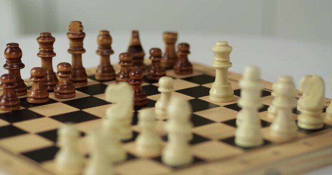 Hand moves chess piece on wooden board. Player plans strategy in intellectual chess game. Focus remains on figures during match. Logic guides every chess move for victory. Smart hobby improves mind.