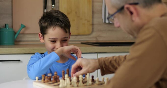 Smart boy makes chess move on board. Kid plays chess game with concentration. Child moves figure in chess game. Strategy and logic education concept.