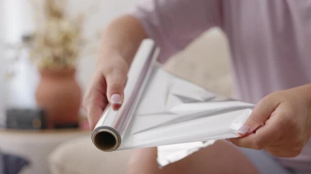 Woman tearing sheet of aluminum foil from kitchen roll for cooking
