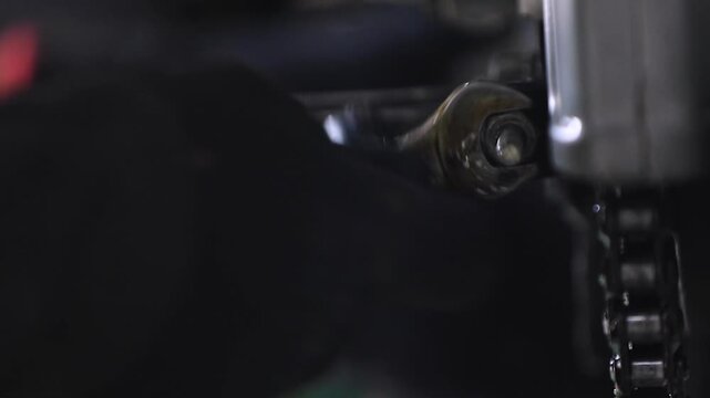 Close-up shot of a mechanic tightening a screw bolt near the motorcycle chain set during maintenance.