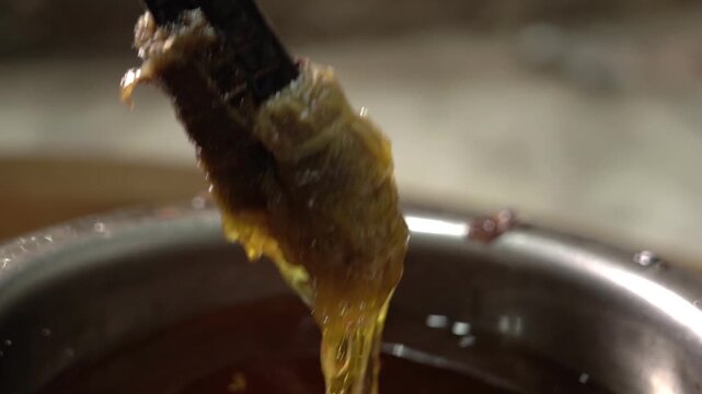Close-up shot of a large bowl filled with ghee used for applying on freshly baked tandoori roti, with a wooden stick placed inside for spreading.