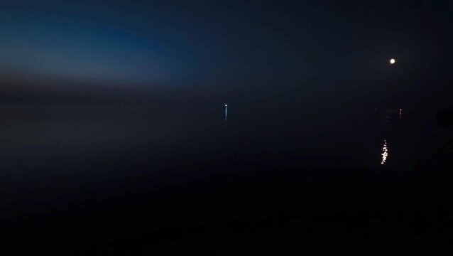 Night scene with calm water and scattered lights from buoys and the moon under a dark sky, view of the North Sea or the Jade Bay at night at the Quermarkenfeuer, Alte Mole in 26382 Wilhelmshaven.