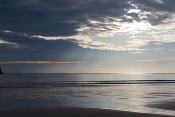 Obraz premium Dramatic sunlight breaking through dark clouds over the ocean and beach.