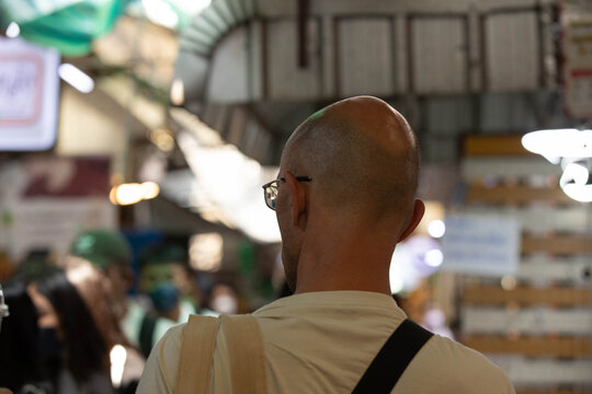 Man with bald head shopping in market, dynamic street life, local vendor street commerce, casual urban walking Thailand, close up, at Wang Lang Market