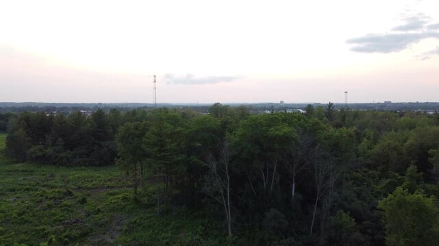 Aerial flight west over trees towards Cambridge, Ontario, Canada during late afternoon just before sunset.
