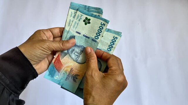 Close-up image of Asian women's hands holding and counting Indonesian rupiah banknotes, while moving the money between their fingers.