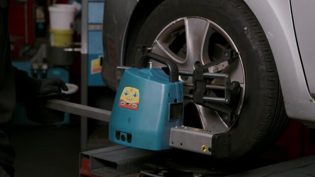Wheel alignment equipment attached to car tire measuring wheel position and angle during vehicle maintenance in automotive service workshop