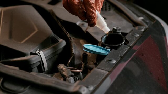 Hand pouring coolant liquid into car radiator reservoir inside engine bay