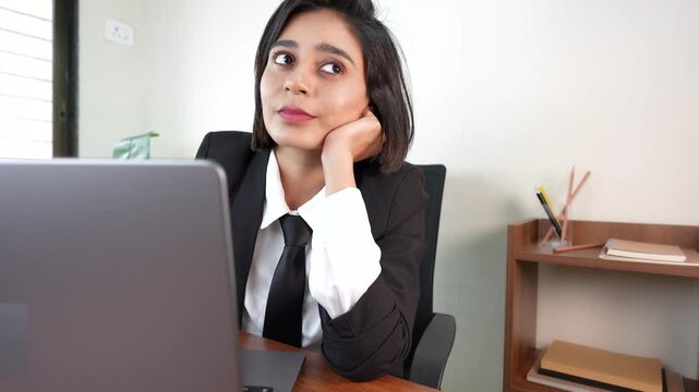 Close up of happy thoughtful young Indian business woman boss manager sits on chair at workplace desk thinking future ideas with positive face expression.
