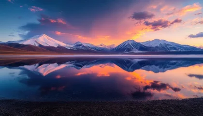 Tableau sur plexiglas Réflexion Snow-covered mountain range reflected in a calm alpine lake under a vibrant pink and orange sunrise sky with scattered clouds and a dark pebbled shoreline, serene and tranquil  © lucky