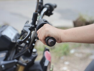An image of a person's hand gripping the handlebars or throttle of a motorcycle.