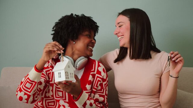 Two joyful friends celebrating their achievement of homeownership while happily holding house keys in their hands. They are excited and embracing the moment of this significant milestone in their