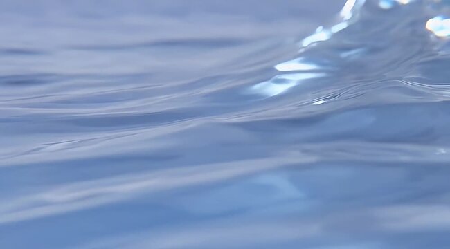 Close-up slow motion video of clear blue water surface with gentle ripples and sunlight reflections, ideal for serene backgrounds or refreshing themes