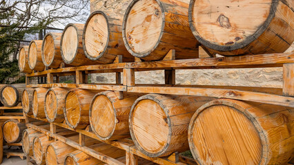 Row of aging wooden barrels storing spirits on racks within an outdoor winery or distillery setting, emphasizing traditional alcohol production and maturation process