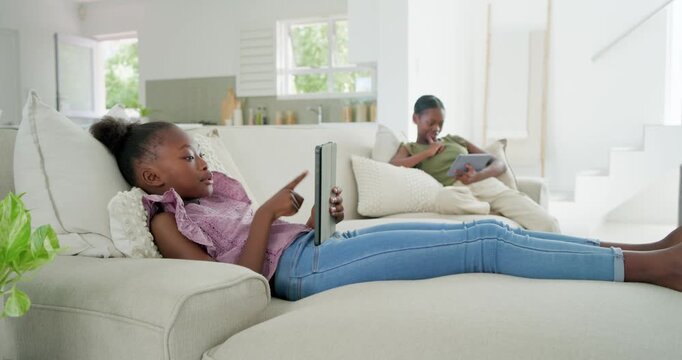 Child on chaise tapping tablet, using education app animation and eliciting sister laughter