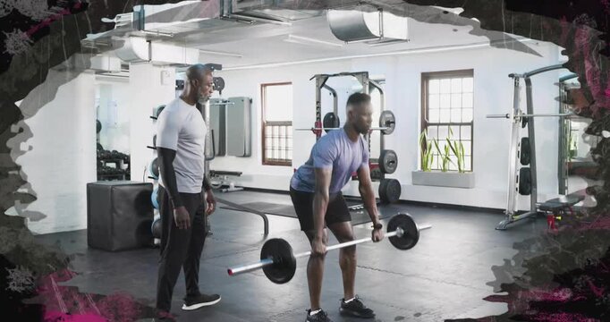 Male trainee gripping barbell and performing deadlifts in gym, trainer monitoring form for strength