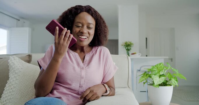 African American woman receiving message, smiling, scrolling and speaking into pink phone on sofa