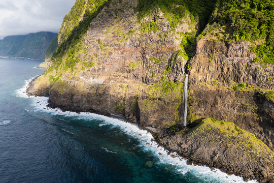 Cascata do Veu da Noiva on Madeira Island featuring a vertical waterfall, rugged cliff face, and ocean waves at the base
