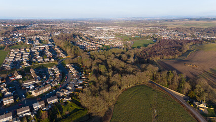Naklejka premium Aerial view of Penicuik nestled in lush greenery: A scenic Scottish townscape surrounded by vibrant fields and woodland in Midlothian