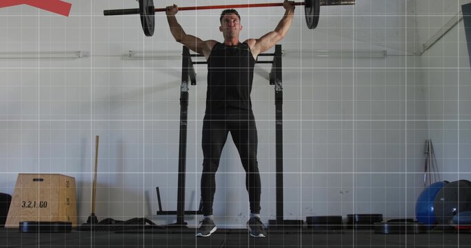 Pressing man holding loaded barbell overhead in garage gym with squat rack, wearing black gear