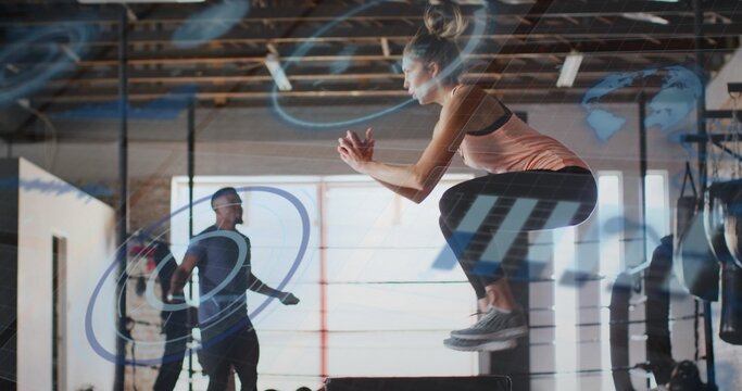 Jumping woman in tank top and leggings performing box jump at gym, with jump rope
