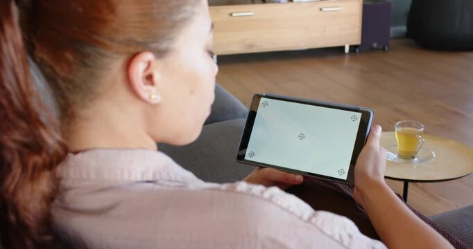 African American woman seeing markers, adjusting tablet angle to align screen on sofa in pale top