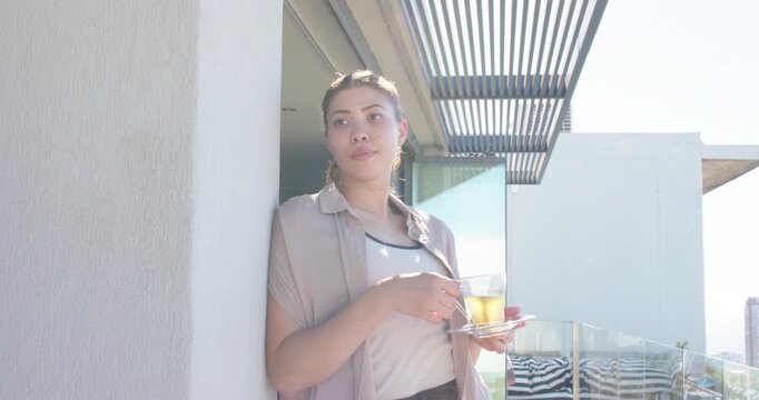 Vertical video: Leaning woman stirring cup with teaspoon on balcony, sunlight drawing gaze