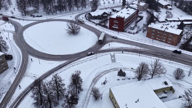 Drone timelapse of trucks navigating a snowy roundabout on icy urban roads, showing winter traffic flow and logistics delays after a storm.