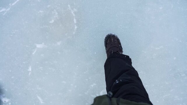 POV feet walking across thin frozen lake ice, showing risky winter travel and danger of falling through. Minimal blue surface with copy space for safety warning concept.