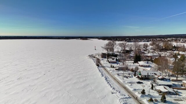 Aerial Drone View of Gosport in Brighton Ontario with Snow Covered Winter Landscape and Ice Over Water Under Blue Sunny Sky