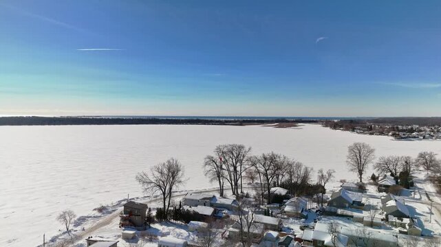 Aerial Drone View of Gosport in Brighton Ontario with Snow Covered Winter Landscape and Ice Over Water Under Blue Sunny Sky