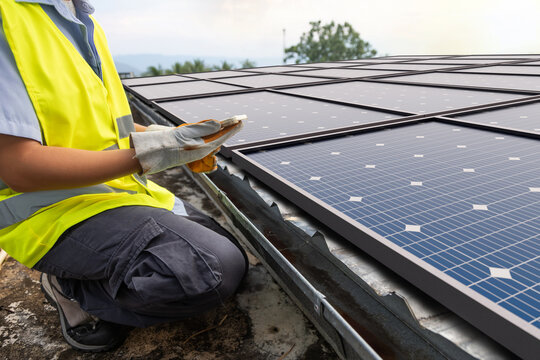 Solar energy technician monitoring photovoltaic system on rooftop with mobile device