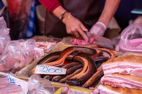 Vendor chopping meat beside tray of eels at market