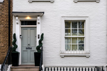 London, UK – A sophisticated grey front door on a white terraced house in Chelsea, featuring ornate spiral topiaries and traditional iron railings, typical of luxury London property design.