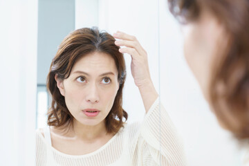 鏡を見て、薄毛を気にするミドルエイジの日本人女性 © gohan