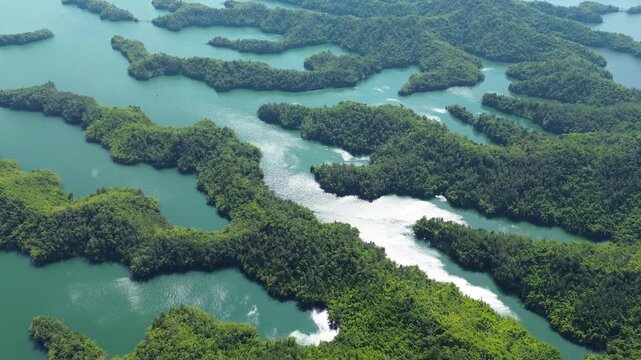 Drone flyover and pan over lush green islands with shimmering water on Ta Dung Lake in Dak Nong, Central Highlands Vietnam. Scenic tropical aerial view of the lake landscape.